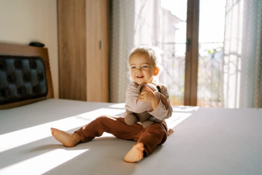 Little happy girl sits on a bed hugging a teddy bear. High quality photo