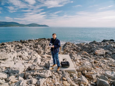 Photographer with a drone in his hands stands on a rocky seashore. High quality photo
