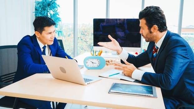 Two business people talk project strategy at office meeting room. Businessman discuss project planning with colleague at modern workplace while having conversation and advice on financial report. Jivy