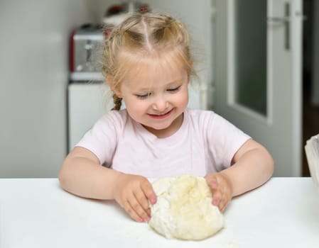 Little girl kneads dough in the kitchen