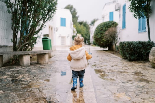 Little girl walks through the puddles in the courtyard. Back view. High quality photo