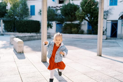 Little laughing girl runs through the tiled courtyard near the house . High quality photo