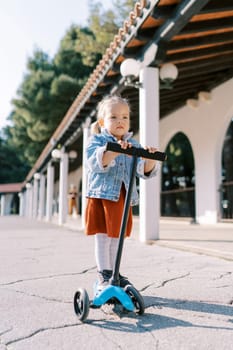 Little girl rides a scooter near a pergola in the park. High quality photo