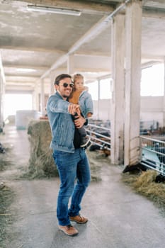 Smiling dad pointing into the distance to a little girl in his arms while standing on a farm. High quality photo
