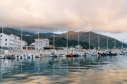 Sailing yachts stand in a row on the pier with colorful villas at the foot of the mountains in the reflections of sunset. High quality photo