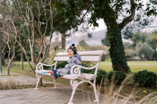 Little whimpering girl in overalls sits on a park bench. High quality photo