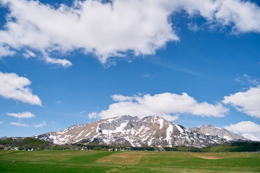 Green pasture at the foot of a mountain range covered with snow. High quality photo