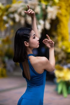 Close-up portrait of a beautiful Asian ballerina posing against the background of a building decorated with flowers