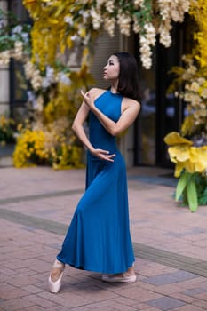 Beautiful Asian ballerina posing against the backdrop of a building decorated with flowers