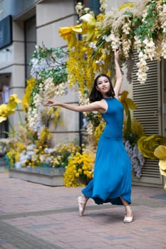 Beautiful Asian ballerina dances against the background of a building decorated with flowers. Vertical photo