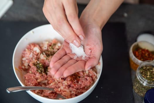 A woman's hand sprinkles salt on a raw meat close-up. Salt is used as a raw meat dressing. High quality photo