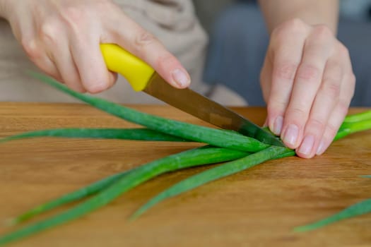 The process of preparing salad. A woman's hand chops a green onion close-up. Salad is used as a side dish for meals. High quality photo.