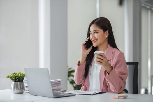 Young businesswoman talking on the phone while sipping coffee in office..