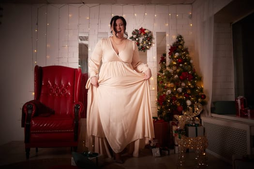 Owerweight elegant Woman at Christmas room. Fat plumb pretty girl in a beautiful dress for a holiday. Buxom female model posing alone in New year sudio