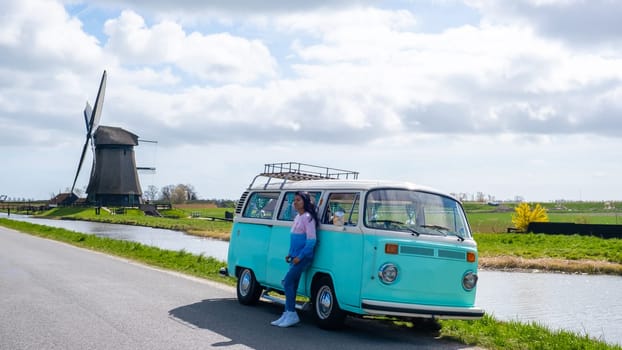 Asian woman doing a road trip with an old vintage car in the Dutch flower bulb region with tulip fields during Spring in the Netherlands