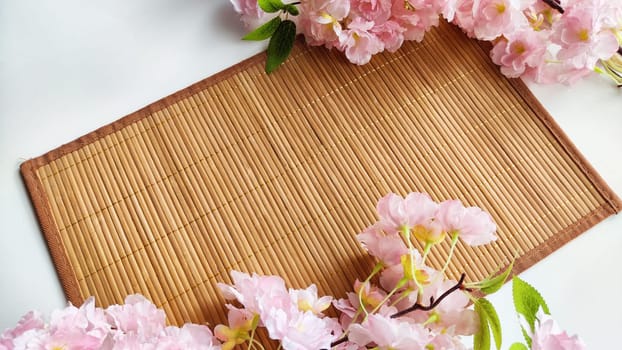 Branch with pink cherry blossom flowers on white background and bamboo napkin or mat. Texture, frame, copy space, background