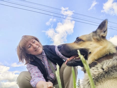 A girl or a woman and a German shepherd or Eastern European Shepherd dog in the forest, in nature, on spring, summer, or autumn day and blue sky. The concept of friendship between humans and animals