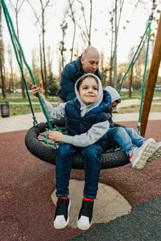 Father swinging his two little sons on a swing on playground in park