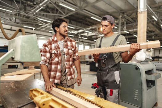 Two young carpenters working with wood standing at table in workshop close up