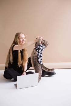 A blogger freelancer in a black is working on a laptop apple and feeds a Scottish straight cat from her hands . blonde assistant in video production with computer MacBook, vertical