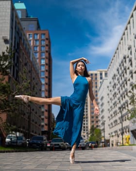 Beautiful Asian ballerina in blue dress posing in splits outdoors. Urban landscape. Vertical photo