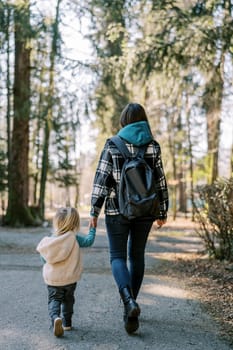 Mom and a little girl walk hand in hand along the road in the forest. Back view. High quality photo