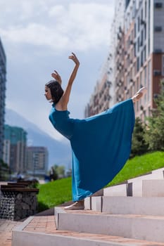 Beautiful Asian ballerina in blue dress posing on stairs outdoors. Urban landscape