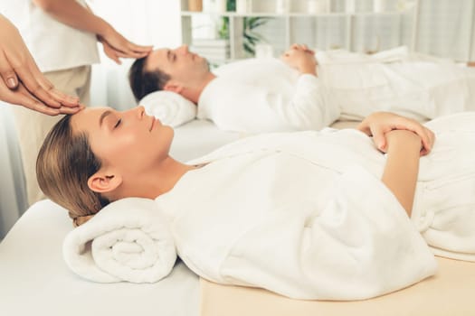Caucasian couple enjoying relaxing anti-stress head massage and pampering facial beauty skin recreation leisure in dayspa modern light ambient at luxury resort or hotel spa salon. Quiescent