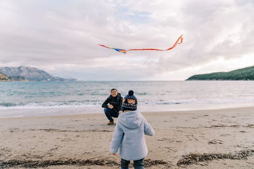 Little girl stands in front of her dad with a kite squatting by the sea. Back view. High quality photo