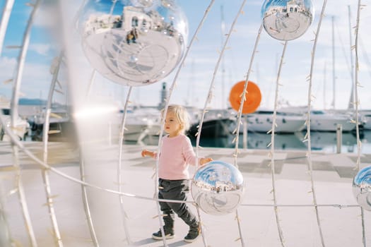 Little girl walks near a Christmas installation with mirror balls. High quality photo