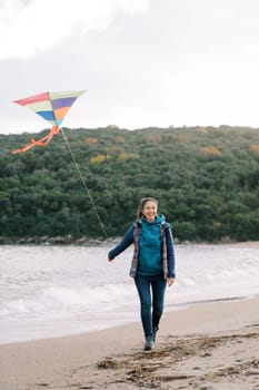 Young smiling woman walking along the seashore with a colorful kite. High quality photo
