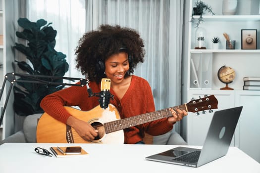 Host channel in musician of young African American playing guitar along with singing, broadcasting on laptop in studio. Decoration of equipment of headsets and recording microphone. Tastemaker.