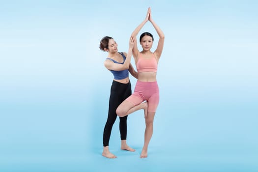 Asian woman in sportswear doing yoga exercise in standing pose with her trainer or yoga buddy. Healthy body care and meditation yoga lifestyle in full shot on isolated background. Vigorous