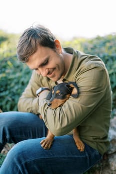 Young smiling man sitting with a puppy on his knees hugging and looking at him. High quality photo