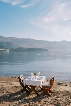 Laid table with chairs stands on a sandy beach by the sea with a view of the mountains. High quality photo