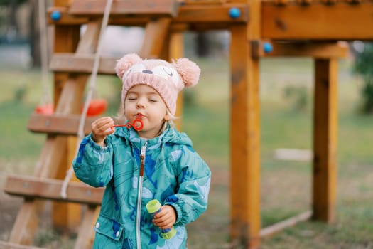 Little girl squinting her eyes and blowing bubbles on the playground. High quality photo