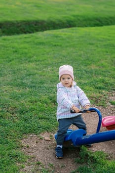 Little girl stands over the seat of a swing-balancer, holding on to the handle. High quality photo