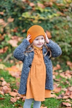A little girl in an orange hat and a gray coat holds in a park