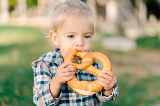 Little girl eating a big pretzel holding it with both hands. High quality photo