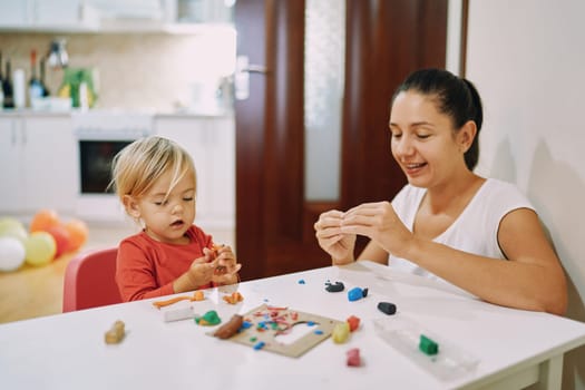 Mom and her little daughter sculpt different figures from plasticine . High quality photo