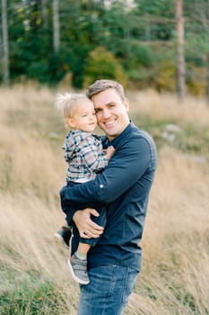 Smiling dad hugging a little girl in his arms while standing in a clearing. High quality photo