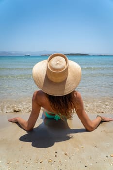 Unknown woman with hat sitting on the beach in front of the sea