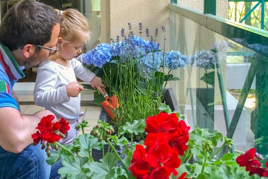 Father and daughter plant flowers on the balcony of the apartment