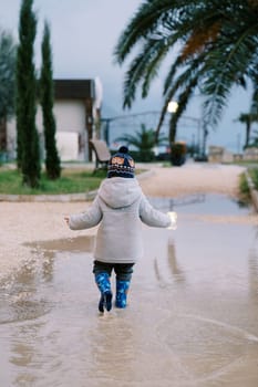 Little girl walks through a puddle looking down at her feet. Back view. High quality photo