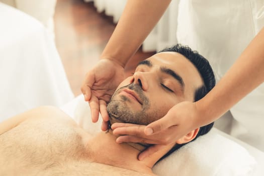 Caucasian man enjoying relaxing anti-stress head massage and pampering facial beauty skin recreation leisure in dayspa modern light ambient at luxury resort or hotel spa salon. Quiescent