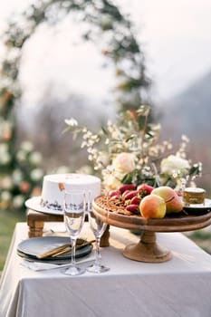 Fruit platter stands near glasses and wedding cake on the table. High quality photo