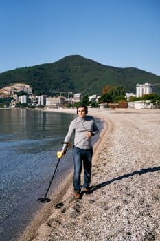 Beach cop runs a metal detector through the shallow sea, listening to headphones. High quality photo