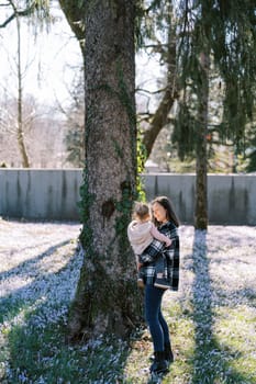 Mom with a little girl in her arms stands near an ivy-covered tree in the park. High quality photo