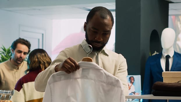 African american man checking shirts on racks in clothing store, looking to buy merchandise from shopping mall. Male client with fashionable lifestyle visiting retail market boutique.