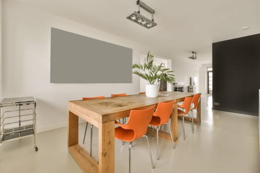 a dining room with orange chairs and a large wooden table in the center of the room is a black wall